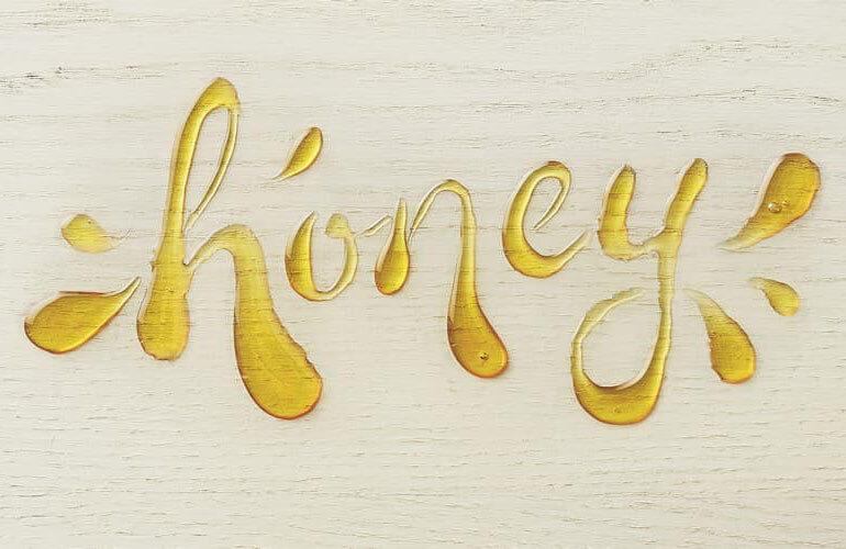 the word honey written with the condiment honey on a wooden board, there are flicks and dashes of honey on both sides of the word to accentuate it
