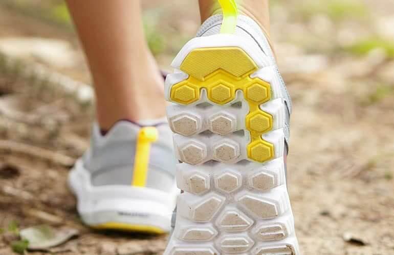 A close-up of a person's athletic shoes walking on a trail.