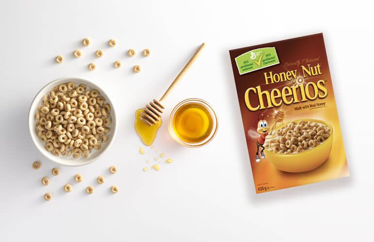 A bowl of honey nut cheerios next to a jar of fresh honey with a Honey Nut Cheerios box.